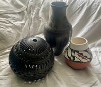 Three pottery items: black spherical cut-out candle lamp, tall black vase, and small painted pot