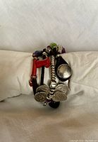 Front view showing the detailed metal coins, beads, and metal loop stamped with brand mark.