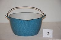Side view of speckled robin egg blue enamelware pot with bail handle and small side handle, showing pour spout, white interior, and signs of wear.