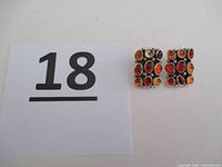Photo showing pair of sterling silver post earrings with nine amber gemstones, next to a card with number 18.