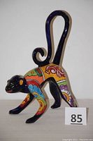 Side angle of the cobalt blue ceramic monkey statue showing the colorful patterns and curled tail.