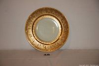 Front view of the porcelain charger plate showing intricate 24K gold-plated design on the rim and white center.