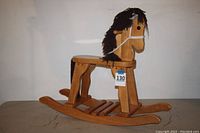 Full side view of wooden rocking horse showing overall structure, seat, curved rockers, yarn mane and tail, rope reins, and a tag labeled 130.
