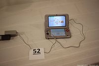 Nintendo 3DS XL gaming device powered on showing Nintendo 3DS Camera screen, connected to charging cord