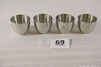 Set of four polished metallic pewter cups placed side by side showing their reflective outer surfaces and round-bottomed style
