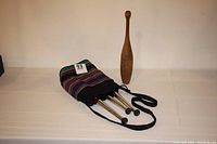 Full view of the set showing three plastic juggling clubs in red, white, and silver colors partially inside a striped cloth carrying bag alongside the vintage wooden juggling club standing upright.