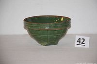 Side view of a green glazed ceramic mixing bowl with square bottom and brown rim.