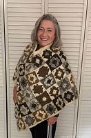 Front view of the handmade wool granny square poncho worn by a model smiling. The poncho is warm and made of crocheted squares in brown, beige, and gray colors.
