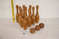 Photo showing ten wooden bowling pins and three wooden balls arranged on a table with a measuring tape showing height.
