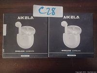 Two boxed sets of Aikela wireless earbuds labeled model S12B on a wooden surface shown side by side.