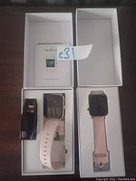 Two pink smart watches in their boxes with user manual and charging cables visible
