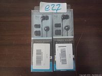 Photo of two individually packaged wired earbuds with iPod branding and additional ear tips visible.