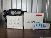 Photo of one LED headlamp resting on its packaging boxes, showing adjustable black strap and icons indicating multiple lighting modes and outdoor activity uses.