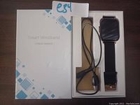 Smart wristband fitness tracker box showing the black watch with gold accents and included charging cable inside the packaging.