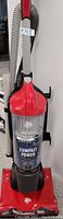 Front view of red and black Dirt Devil Endura Reach Compact Power upright vacuum with detachable hose on the side and long handle extending upwards.