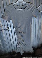 Photo of grey Jed North short-sleeved ruched scoop neck dress hung on a hanger against a metallic background.