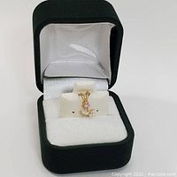 Front view of the 10kt gold flower pendant inside a green and white jewelry display case.