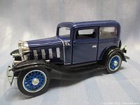 Side view of the 1932 Chevy Standard Coach Car die-cast model showing blue and black paint, spoked blue wheels, and chrome details.