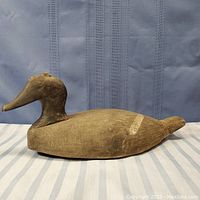 Side profile of antique duck decoy showing carved body, painted surface with visible wear and scratches.