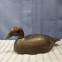 Side profile of the wooden duck decoy showing overall shape and worn dark paint with carved details.
