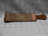Leather razor strop displayed flat with wooden handle, showing wear and supple leather.