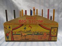 Full front view of the wooden Eagle Big Show pencil display with nine colored pencils inserted in top slots, show antique circus scene.
