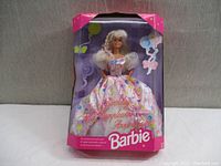 Front view of boxed Barbie doll in pink dress with birthday balloon and bow graphics on packaging.