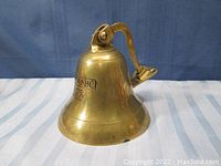 Full view of brass bell with wall mount bracket against blue background.
