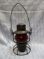 Full view of vintage kerosene lantern with red globe and protective wire cage with hanging handle.