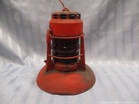 Full view of the red Dietz No. 40 lantern showing its metal base, glass globe, and protective wire cage.