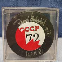 Front view of black hockey puck with CCCP 72 logo and Frank Mahovlich signature, H.O.F 81 and #27 inscription.