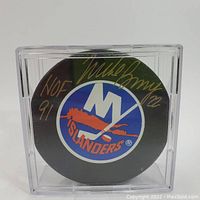 Front view of signed New York Islanders hockey puck with visible autograph and logo inside plastic display case.