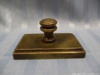 Angled top view of solid brass paperweight showing handle and base condition with patina and wear marks.