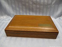 Closed view of the wooden jewelry box showing its polished surface and brass plate on the lid.