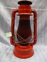 Full view of red metal lantern with red crescent-shaped glass lens and protective wire framing, showing overall good condition.