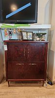Full front view of antique wooden sewing cabinet with TV on top and decorative items.