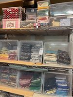 Shelf holding multiple clear plastic bins each filled with neatly folded fabric pieces in assorted colors and patterns