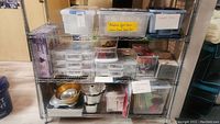 Wide view of bottom three shelves showing various labeled and unlabeled plastic containers and bins with baking molds, cake supports, and other baking tools.