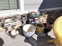 Photo showing nine ceramic planter pots arranged on two metal plant stands and on the ground, including a white ceramic cat figurine yard art piece
