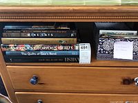 Stack of seven coffee table books arranged horizontally on a wooden shelf, showing spines with titles related to national parks, cats, Cartier, and quilts.