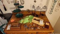 Wooden table with assorted brooches and necklaces, a black metal cat-themed jewelry holder, and a wooden box with winged pins