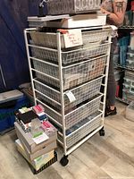 Full view of the white metal rolling rack with six wire mesh drawers filled with jewelry making supplies and craft items.