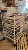 Three photos showing the white Elfa rolling wire storage organizer from different angles. Includes five wire mesh drawers and caster wheels. Unit is lightly used and contains no items inside the drawers.