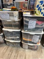 Stack of clear plastic storage bins filled with various fabrics and sweaters, labeled with contents like 'Old Wool Sweaters CATS' and 'Animal making FUR Wool Faux Suede'