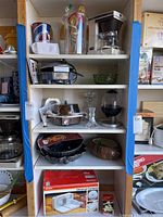 Five wooden shelves stocked with kitchen items including coffee maker, glass bowl, egg cooker, tiered metal tray, and boxed Krups food slicer.
