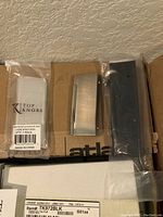 Box containing multiple cabinet pulls in flat black and brushed nickel finishes, with original packaging and shipping/order form visible