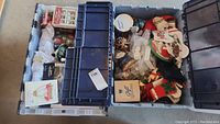 Overhead view of two large plastic totes filled with Christmas decorations, including glass ornaments, stockings, and figurines