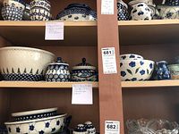 Multiple Polish pottery pieces displayed on wooden shelves including large bowl, canisters, creamer, sugar bowl, small cups and a glass bowl.