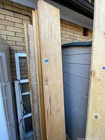 Stack of 8 wooden shelving boards leaning against a shed with visible width and length.