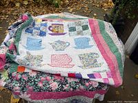 Folded quilt showing teacup and teapot applique pattern on top with floral patchwork borders